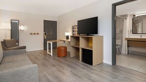 A modern living room with a sofa, a TV, a small table, and a cabinet. - Spark by Hilton Rock Springs (Rock Springs)