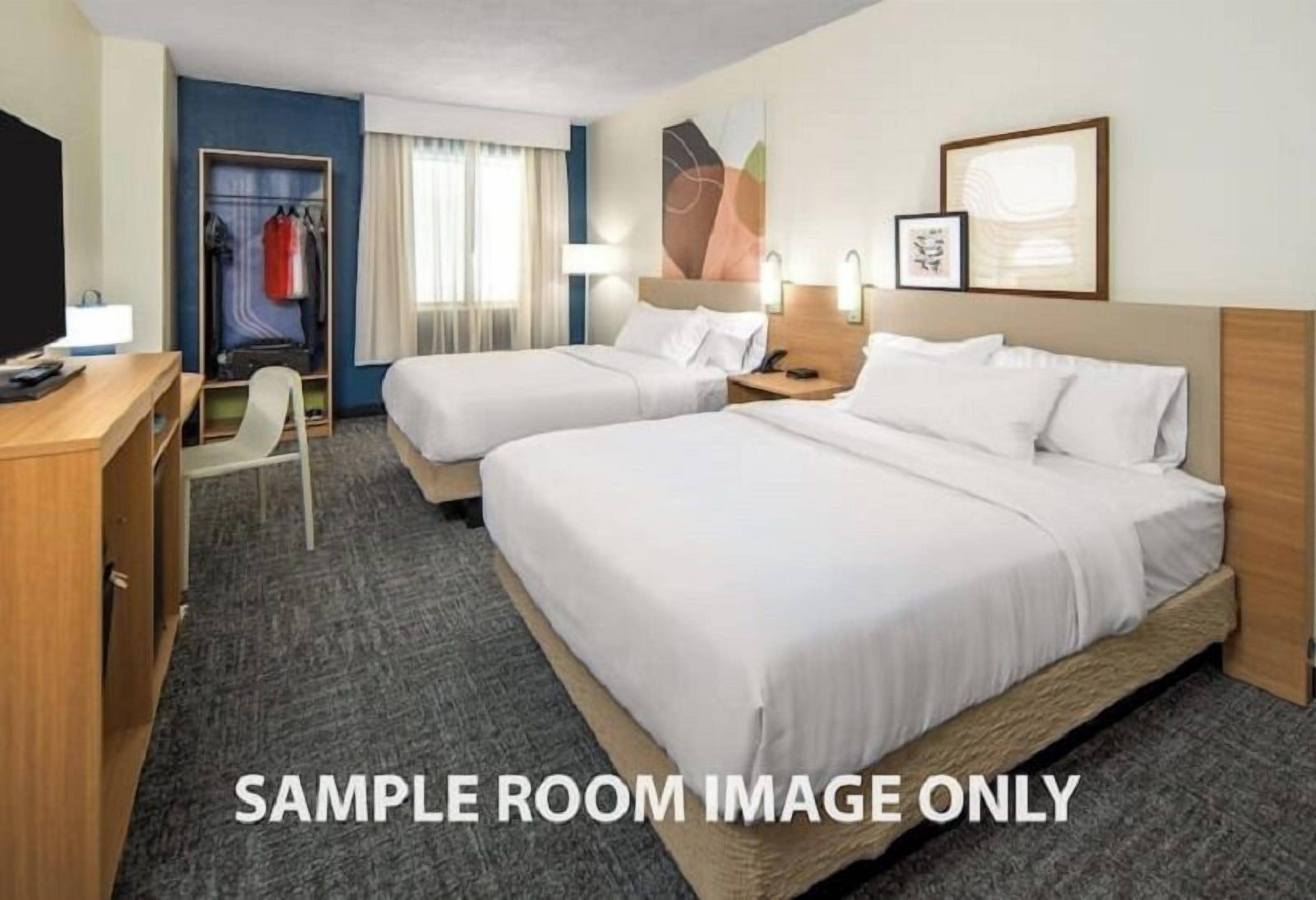 A sample hotel room with two beds, a desk, a chair, a wardrobe, and a television.