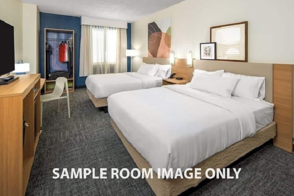 A sample hotel room with two beds, a desk, a chair, a wardrobe, and a television.