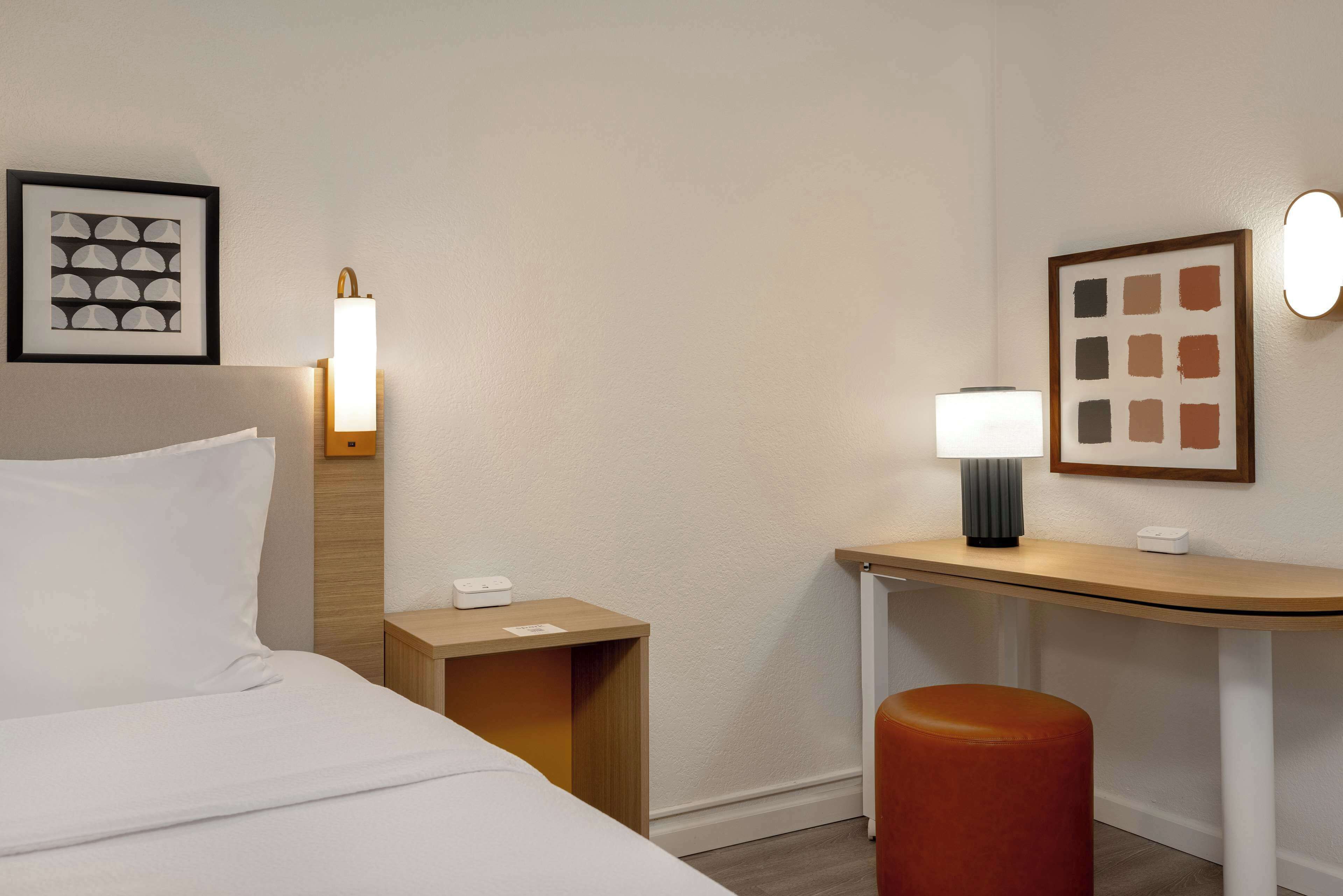 Een hotelkamer met een bed, een bureau, een stoel, een nachtkastje en twee wandlampen.
