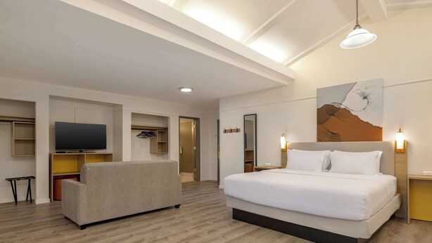 A hotel room with a large bed, a sofa, a TV, and a painting on the wall. - Spark by Hilton Rock Springs (Rock Springs)