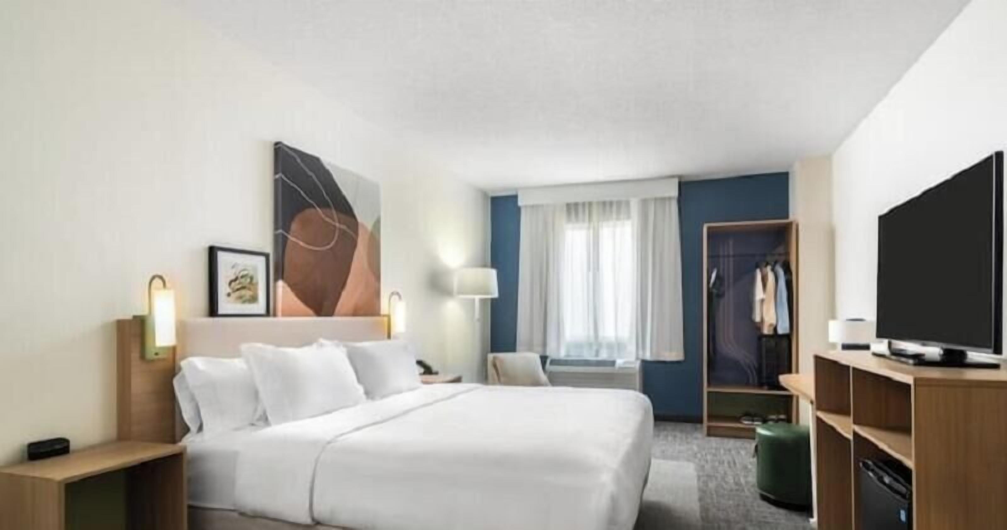 A hotel room with a bed, bedside tables, a TV, a wardrobe, and a window with curtains.