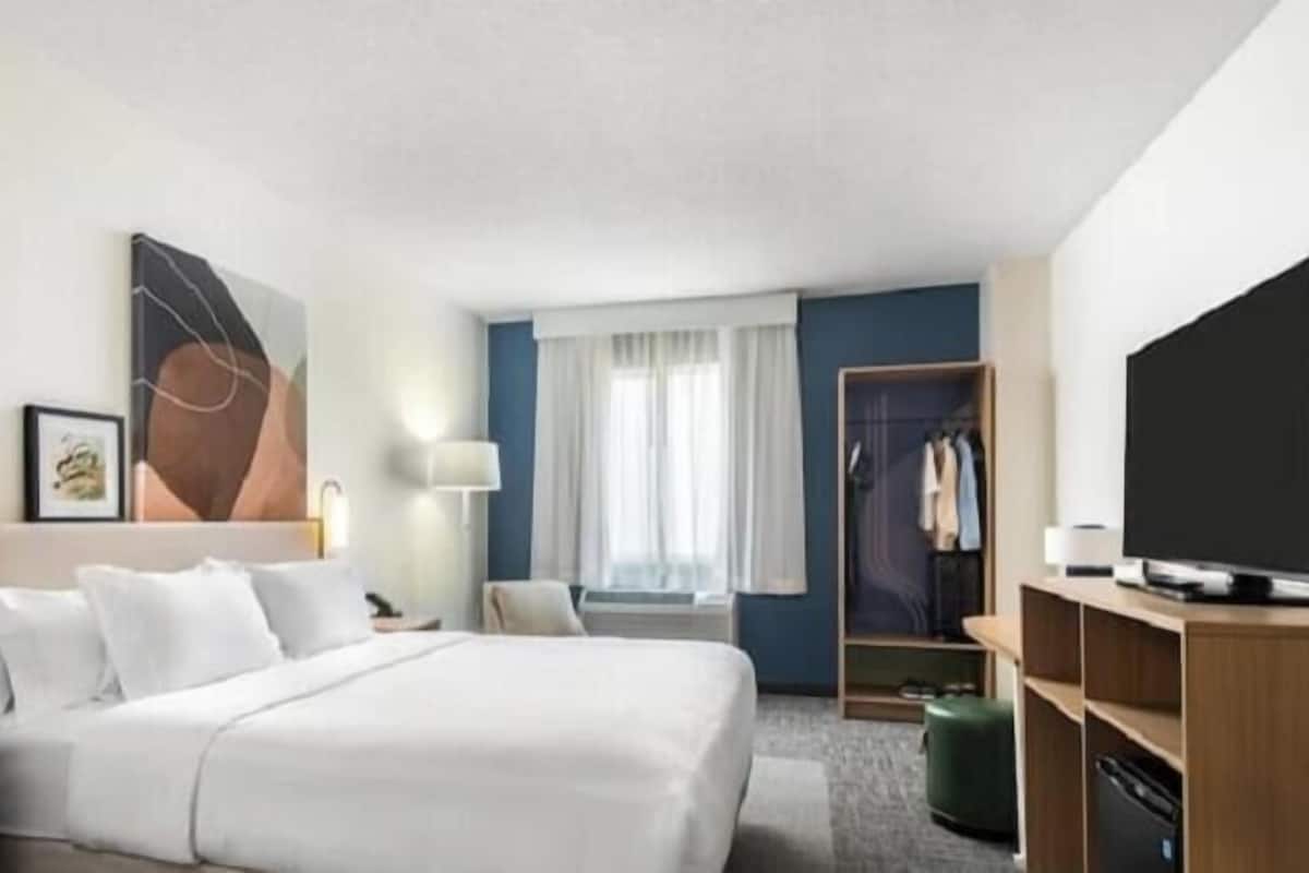 A hotel room with a bed, bedside tables, a TV, a wardrobe, and a window with curtains.