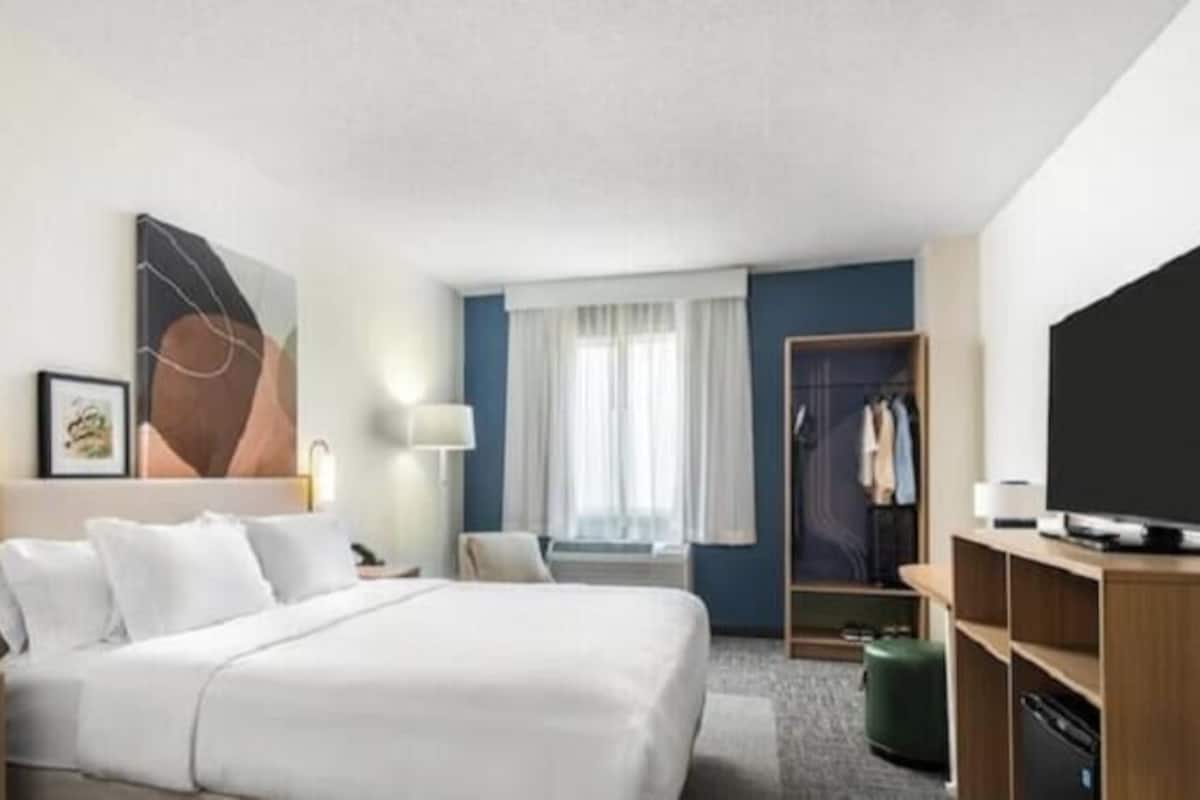 A hotel room with a bed, bedside tables, a TV, a wardrobe, and a window with curtains.