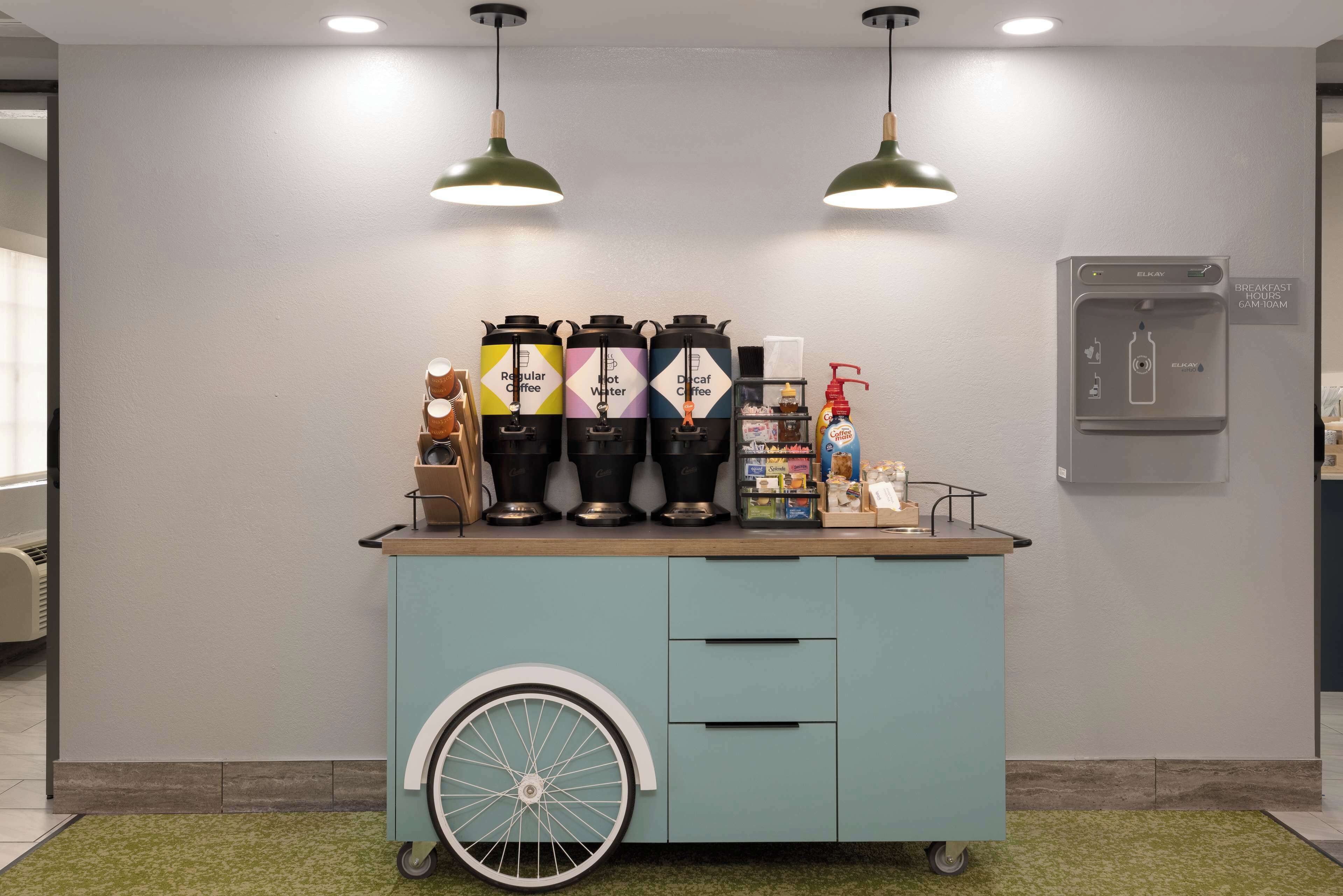 Een koffiehoek met meerdere koffieautomaten, een waterkraan en een ontbijtbuffet in de hotelentree.
