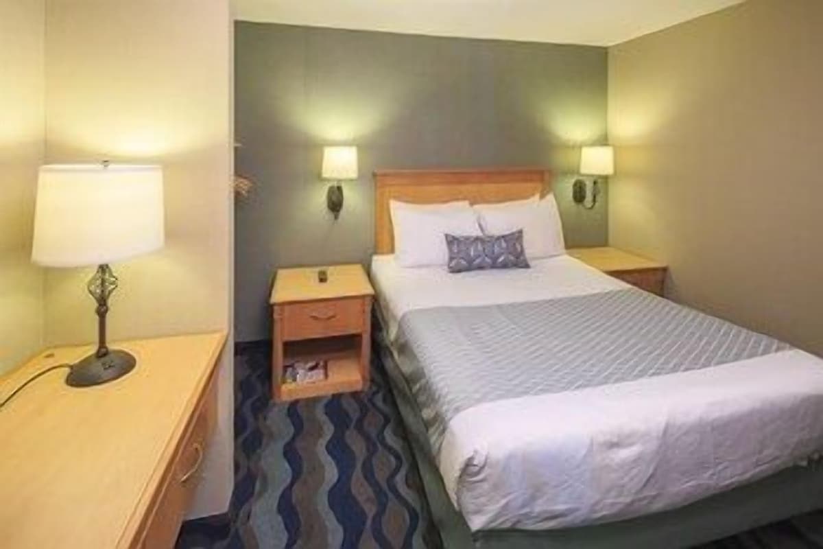 A hotel room with a bed, two bedside tables, a nightstand, a lamp, and a wall-mounted light.