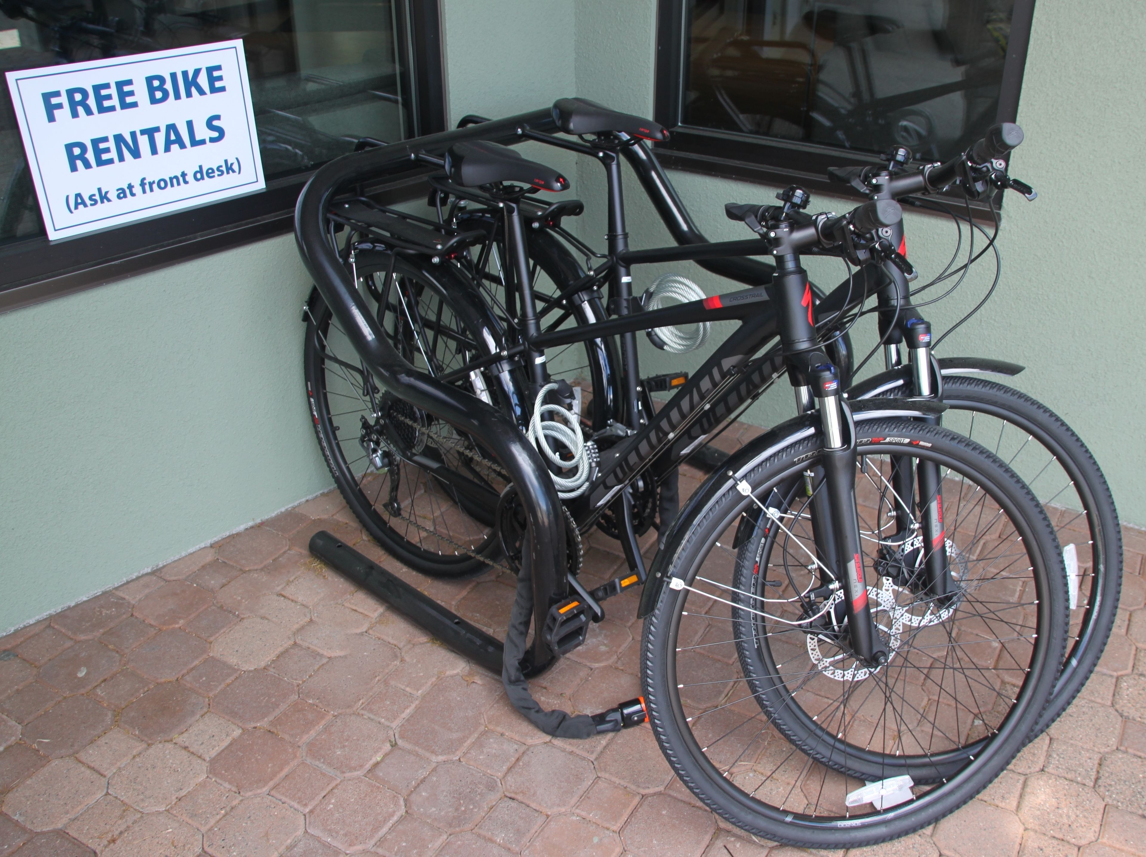 A bicycle secured to a rack outside a building with a sign indicating free bike rentals.