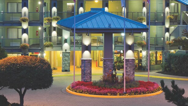A hotel with a prominent Accent Inn sign, multiple balconies, and a well-lit entrance area. - Accent Inns Vancouver Airport (Richmond)