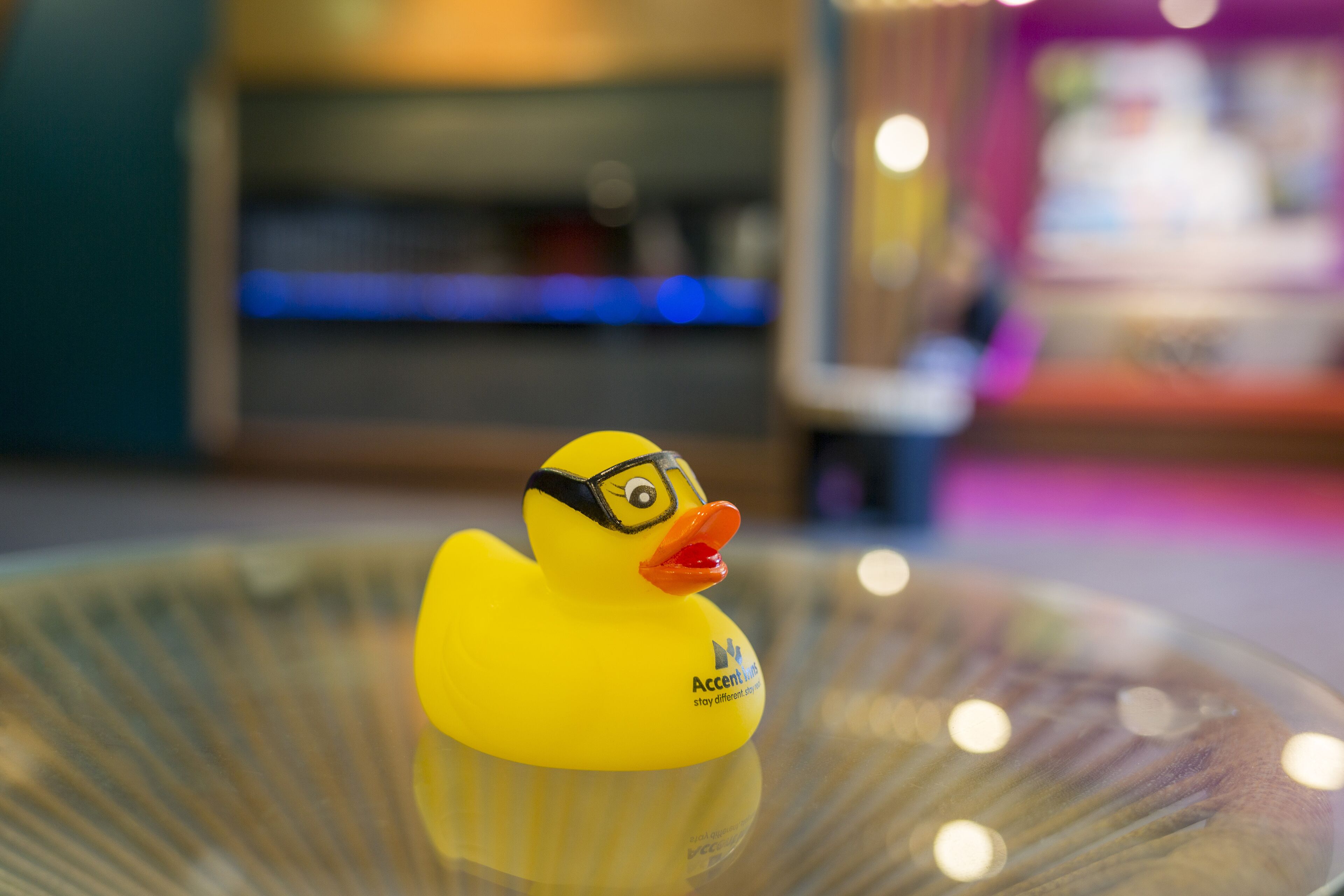 A yellow rubber duck with glasses and a red beak on a glass surface.