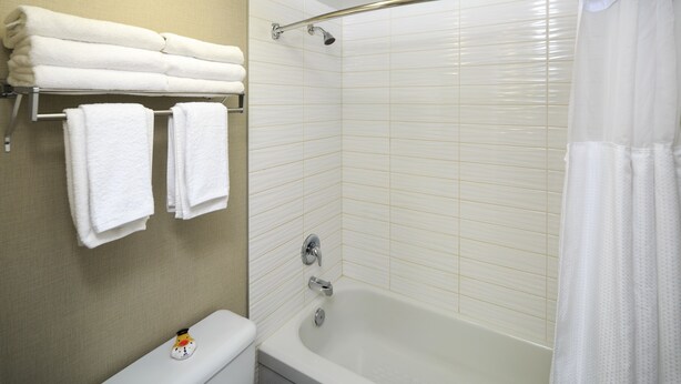 A bathroom with a bathtub, a toilet, and a towel rack with folded towels.
