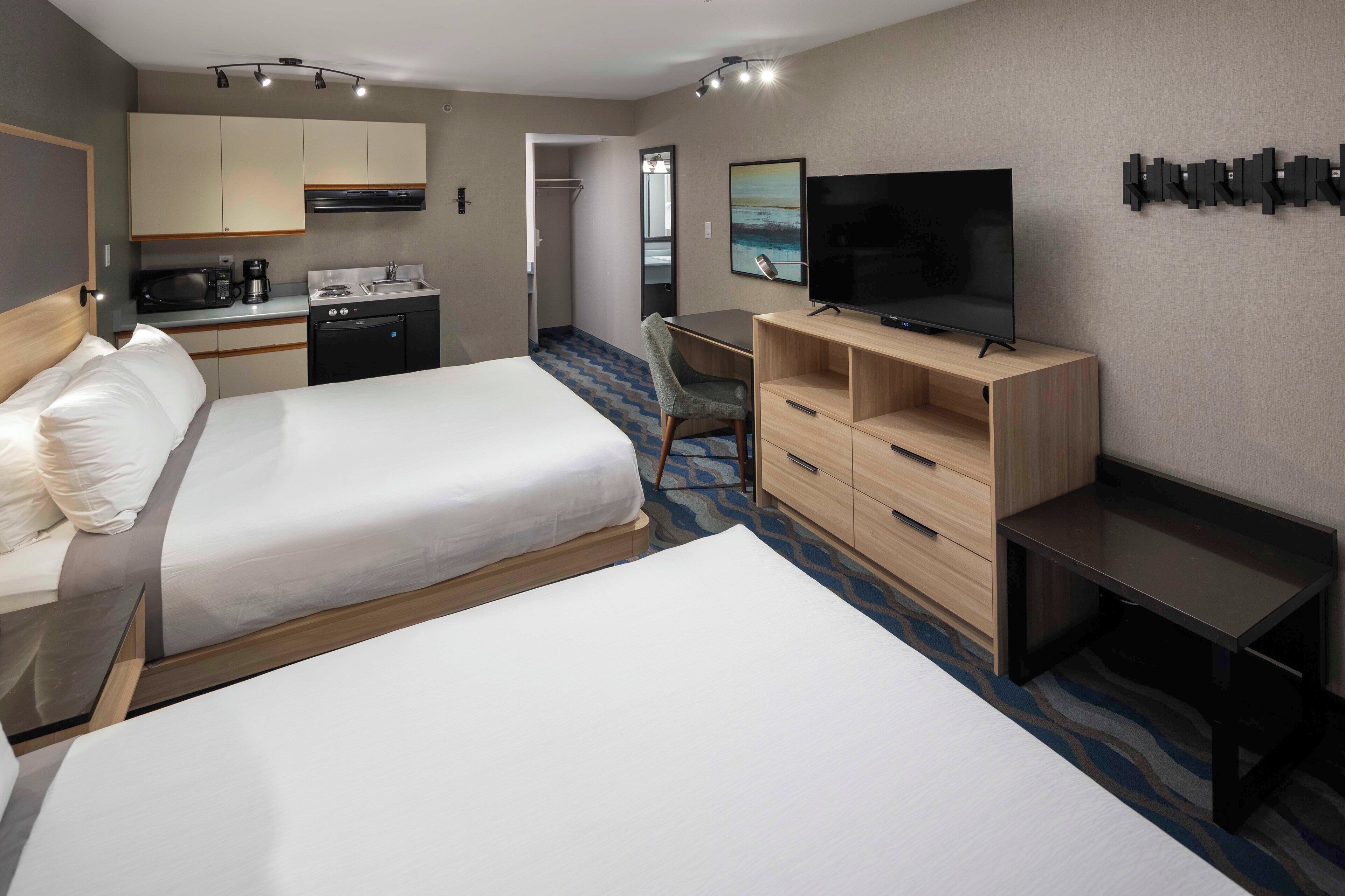 Una habitación de hotel con dos camas, un escritorio, televisión y una kitchenette.