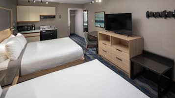 Een hotelkamer met twee bedden, een bureau, een televisie en een kitchenette.