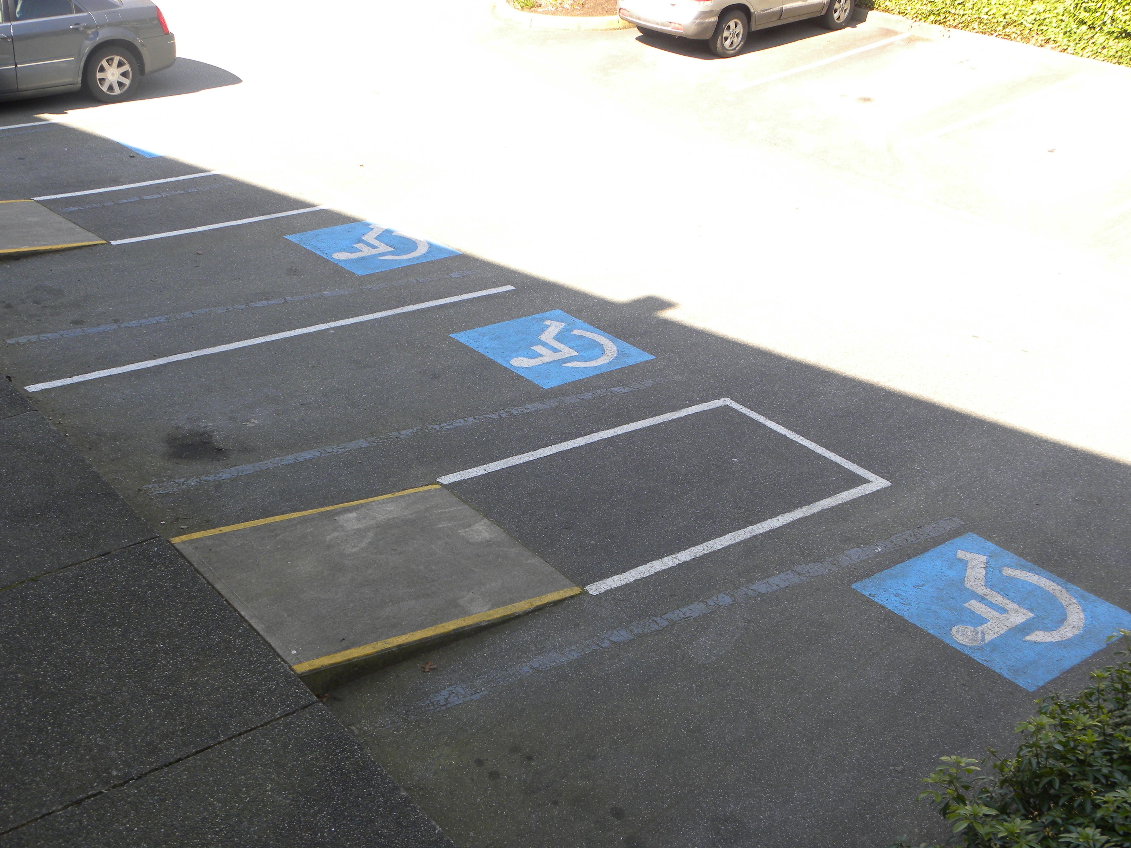 Un estacionamiento con espacios reservados para discapacitados señalizados con pintura azul y símbolos de sillas de ruedas.