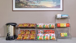 A kitchenette with a coffee maker, shelves stocked with Kellogg's and Twinings' breakfast cereals, and a painting on the wall. - Tumut Farrington Motel (Tumut)