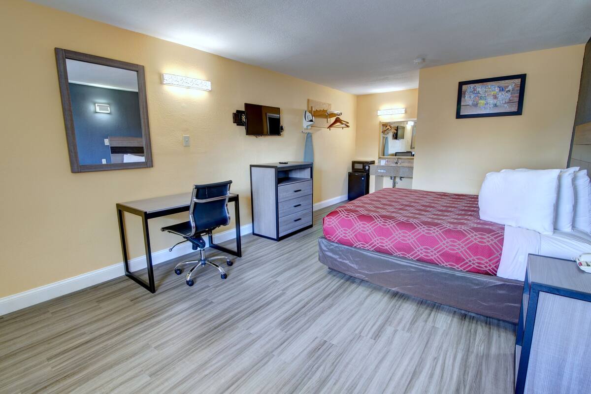 A hotel room with a bed, desk, chair, dresser, and a mirror.