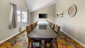 A conference room with a long table, chairs, a flat-screen TV, and a clock on the wall.