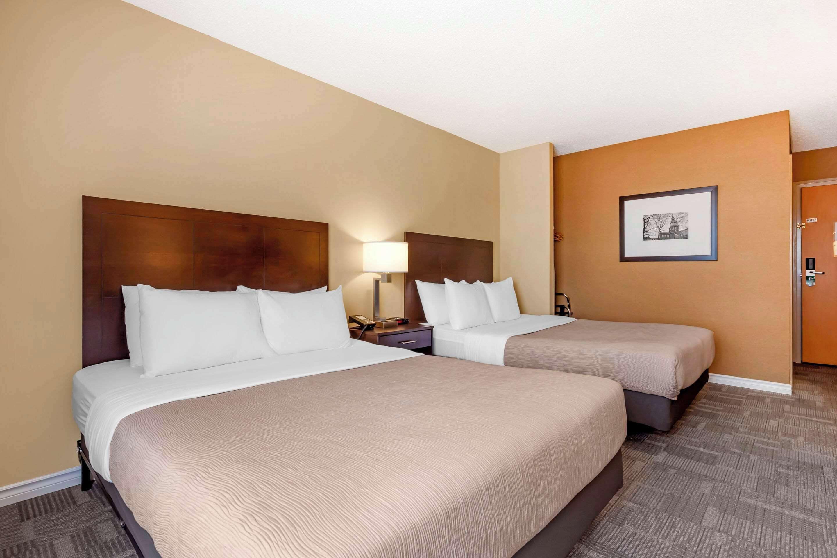 A hotel room with two beds, a nightstand with a lamp, and a framed picture on the wall.