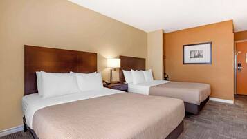 A hotel room with two beds, a nightstand with a lamp, and a framed picture on the wall.