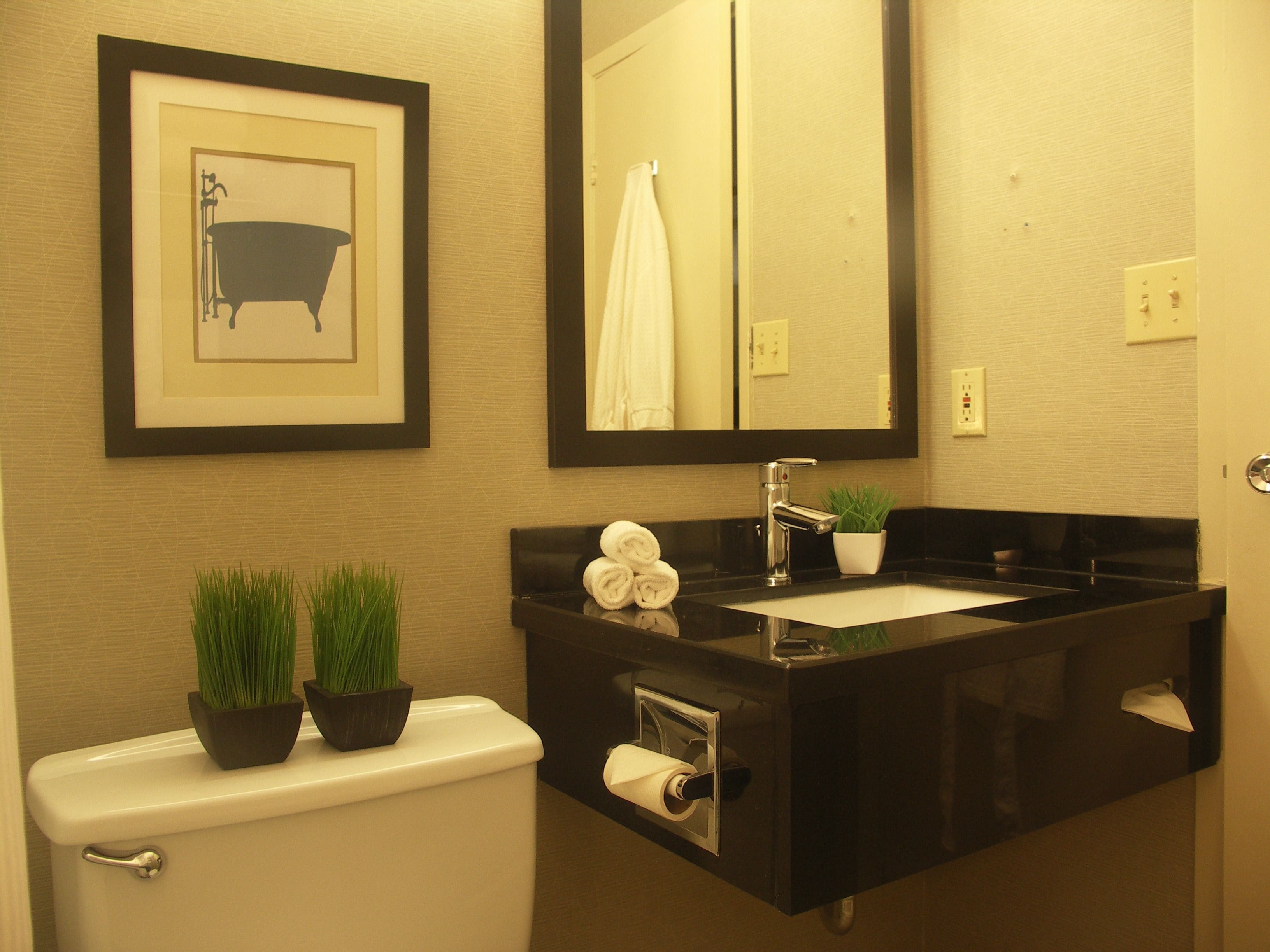 Un baño moderno con un lavamanos negro, un inodoro y un cuadro con una bañera.