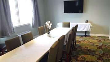 A conference room with a long table, chairs, a potted plant, a flat-screen TV, and a patterned carpet.