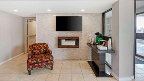 A reception area with a sofa, a flat-screen TV mounted on the wall, a coffee machine, and a counter with various items.