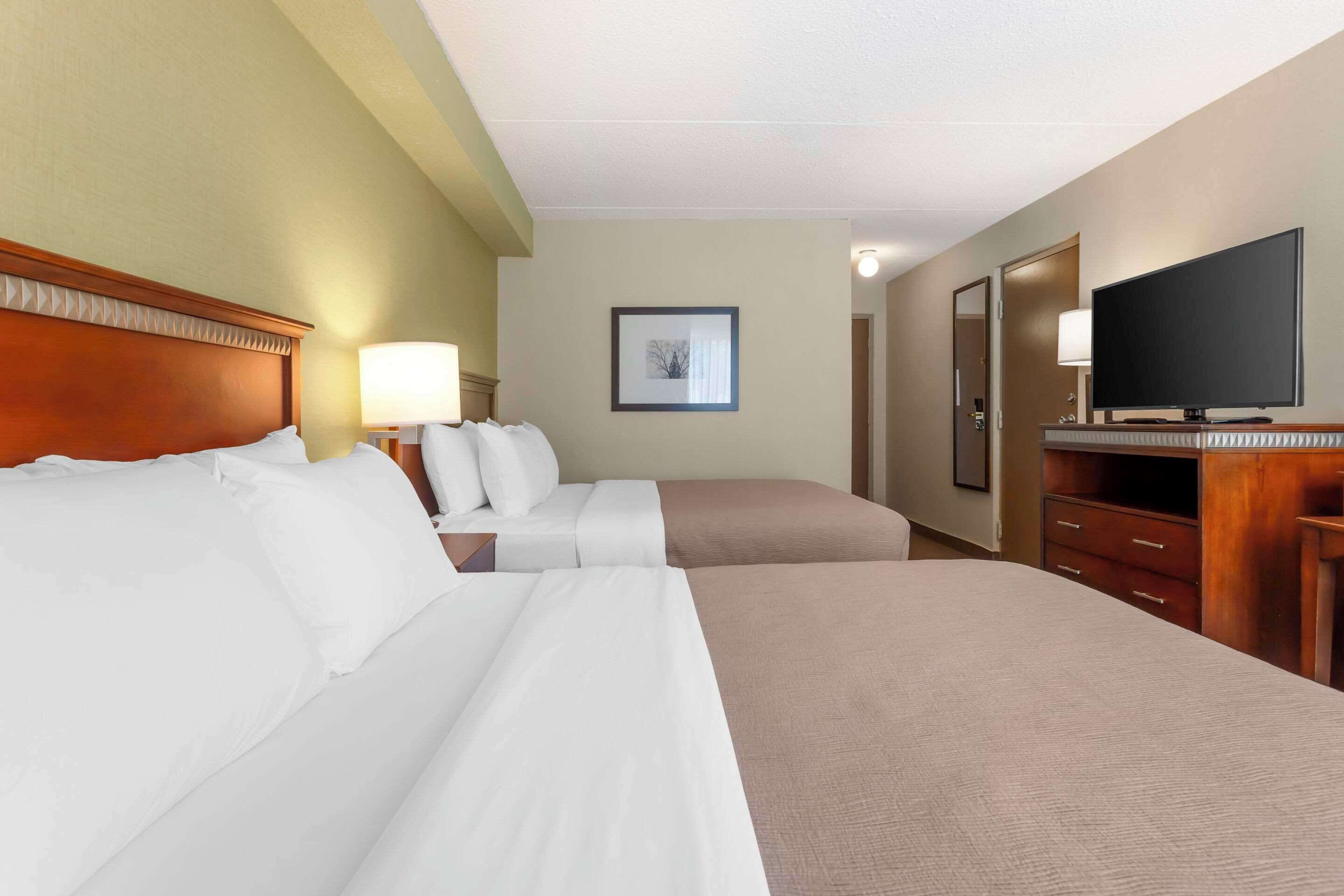 A hotel room with two beds, a TV, a desk, and a framed picture on the wall.