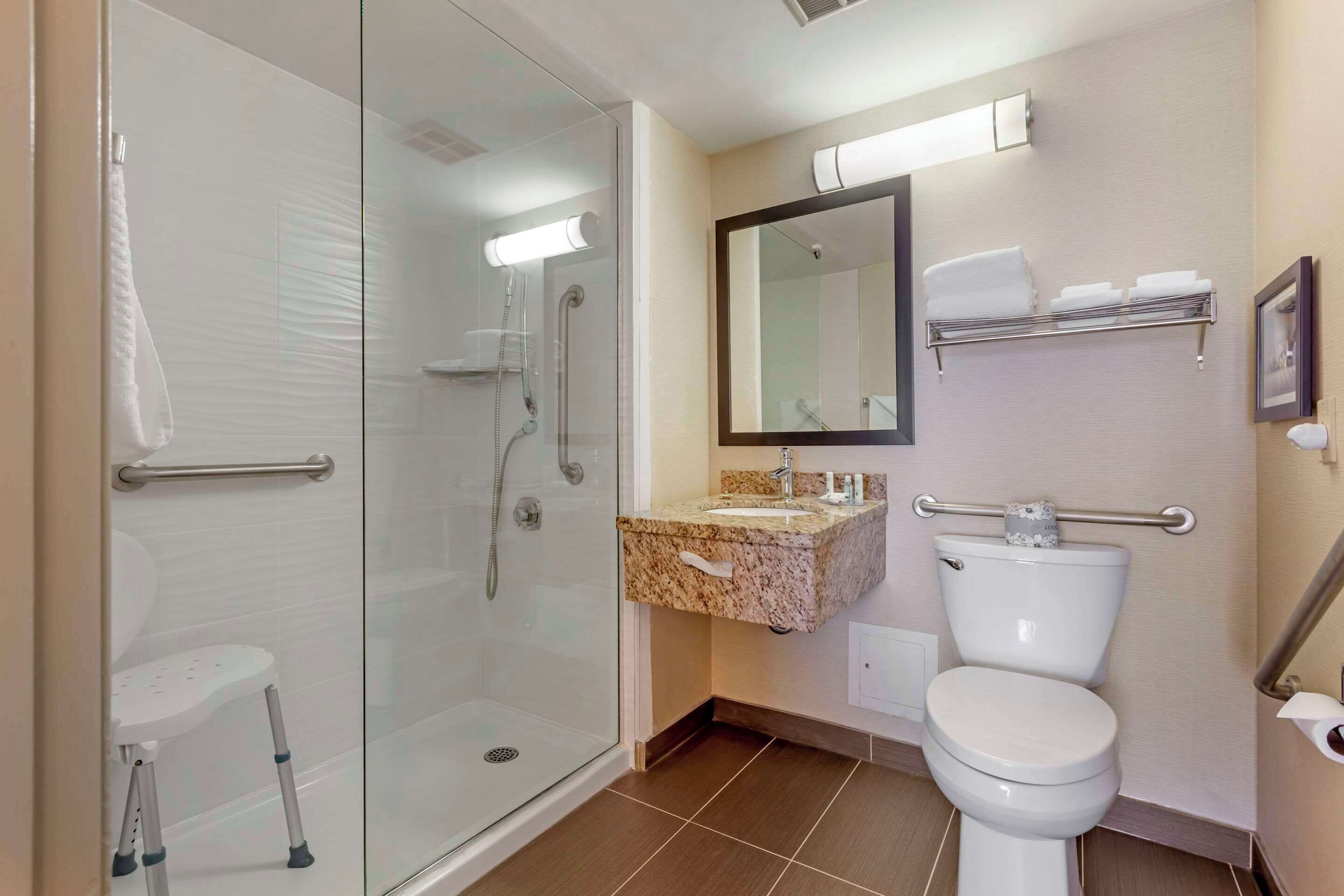 Une salle de bain moderne avec une douche à parois de verre, des toilettes blanches, un lavabo en granit et un miroir au-dessus du lavabo.