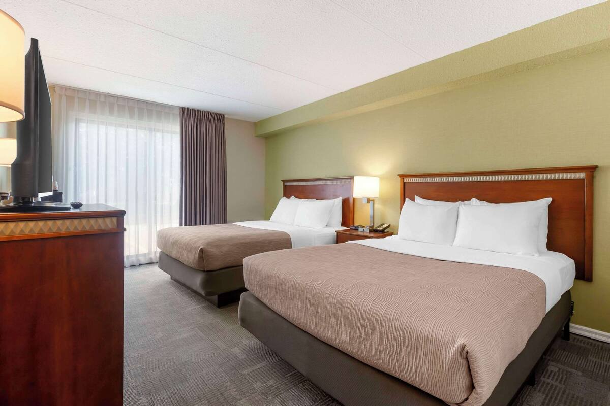 A hotel room with two beds, a desk with a television, and a window with curtains.