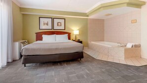 A hotel room with a large bed, a separate bathroom with a bathtub, and two framed pictures on the wall.