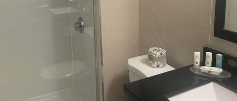 Un baño con ducha de vidrio, inodoro y lavamanos con artículos de aseo.