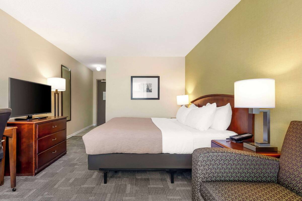 A hotel room with a bed, a TV, a desk, and a chair.