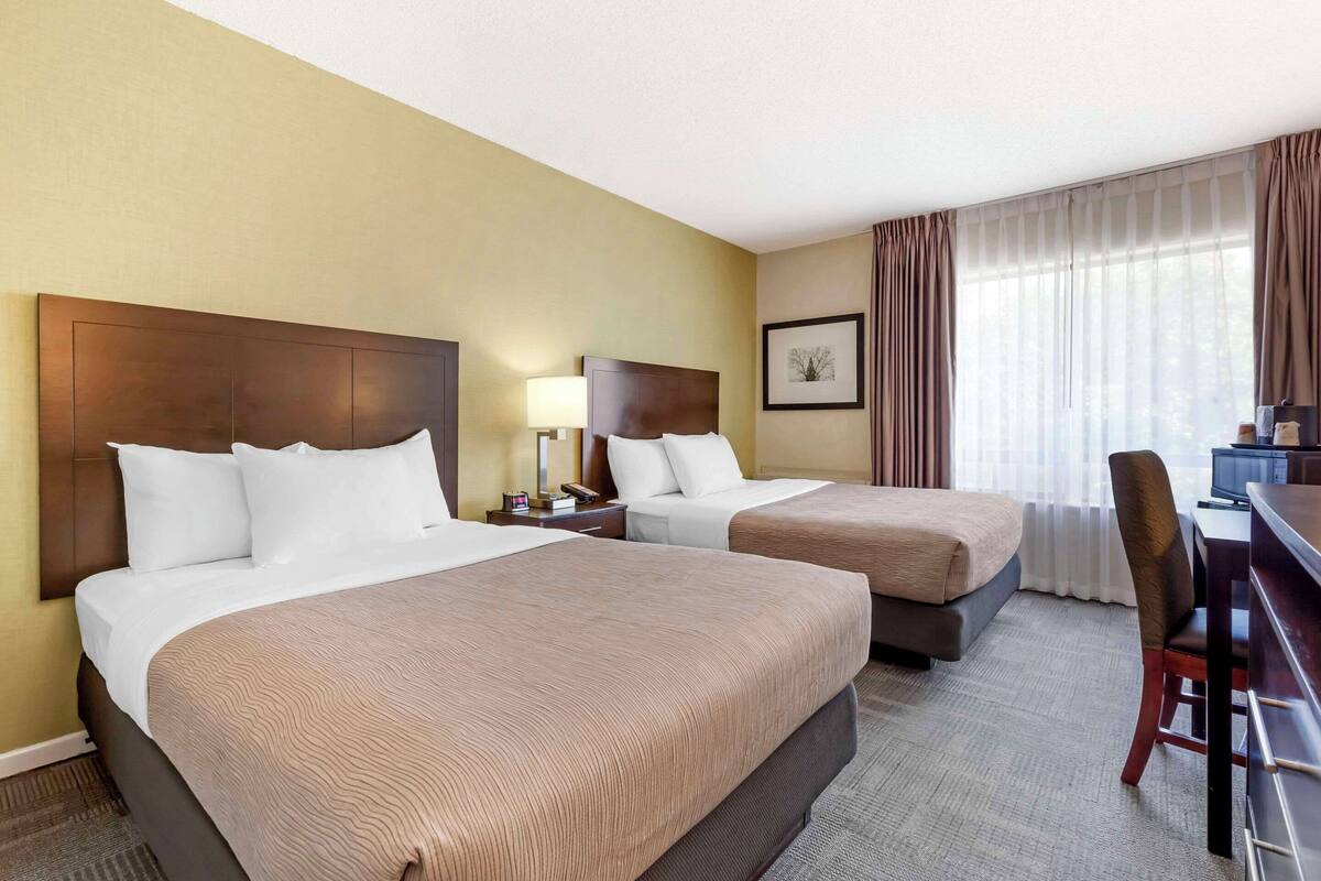 A hotel room with two beds, a desk, and a chair.