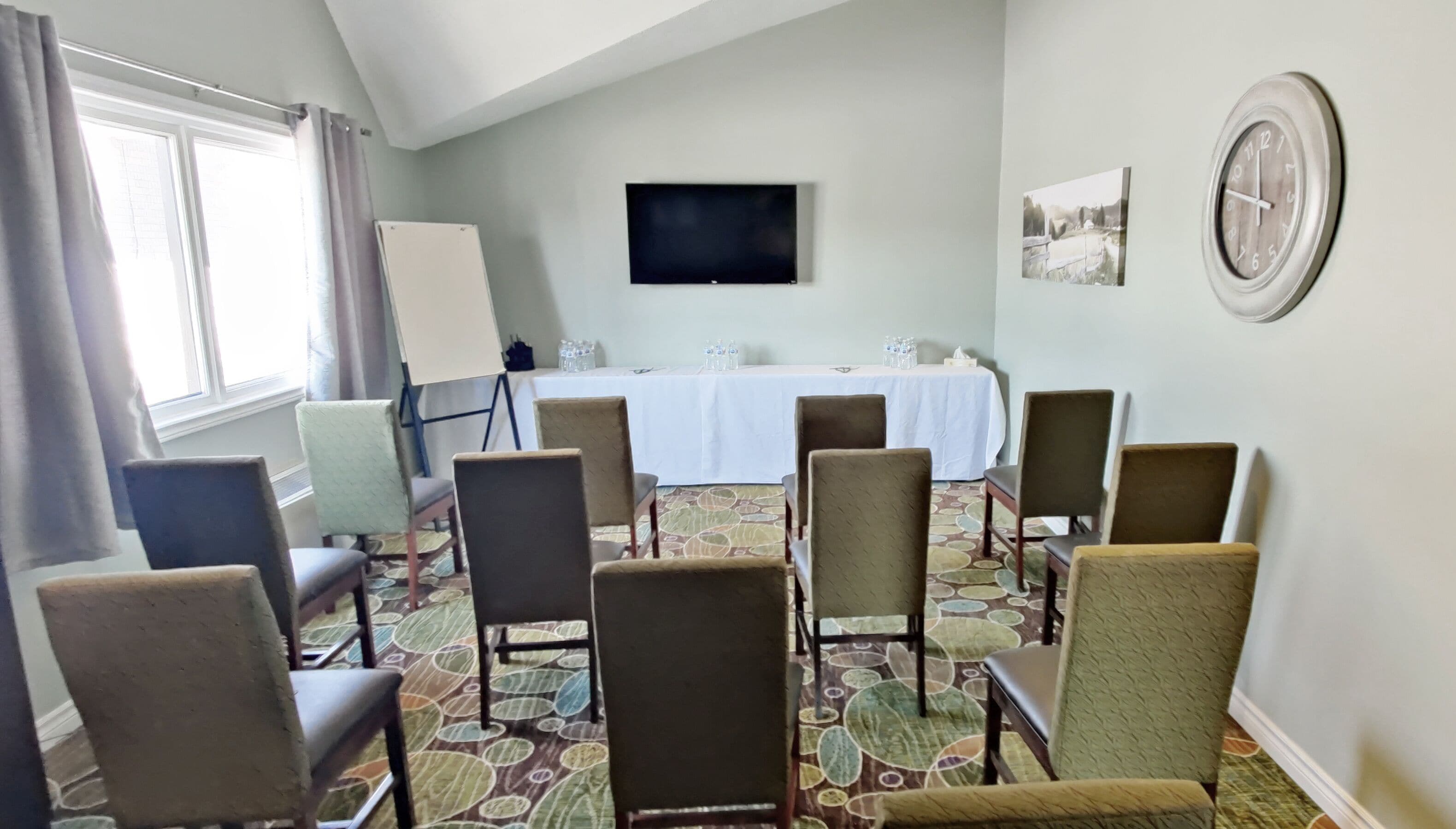 A conference room with a white table, chairs, a flat-screen TV, and a painting on the wall.