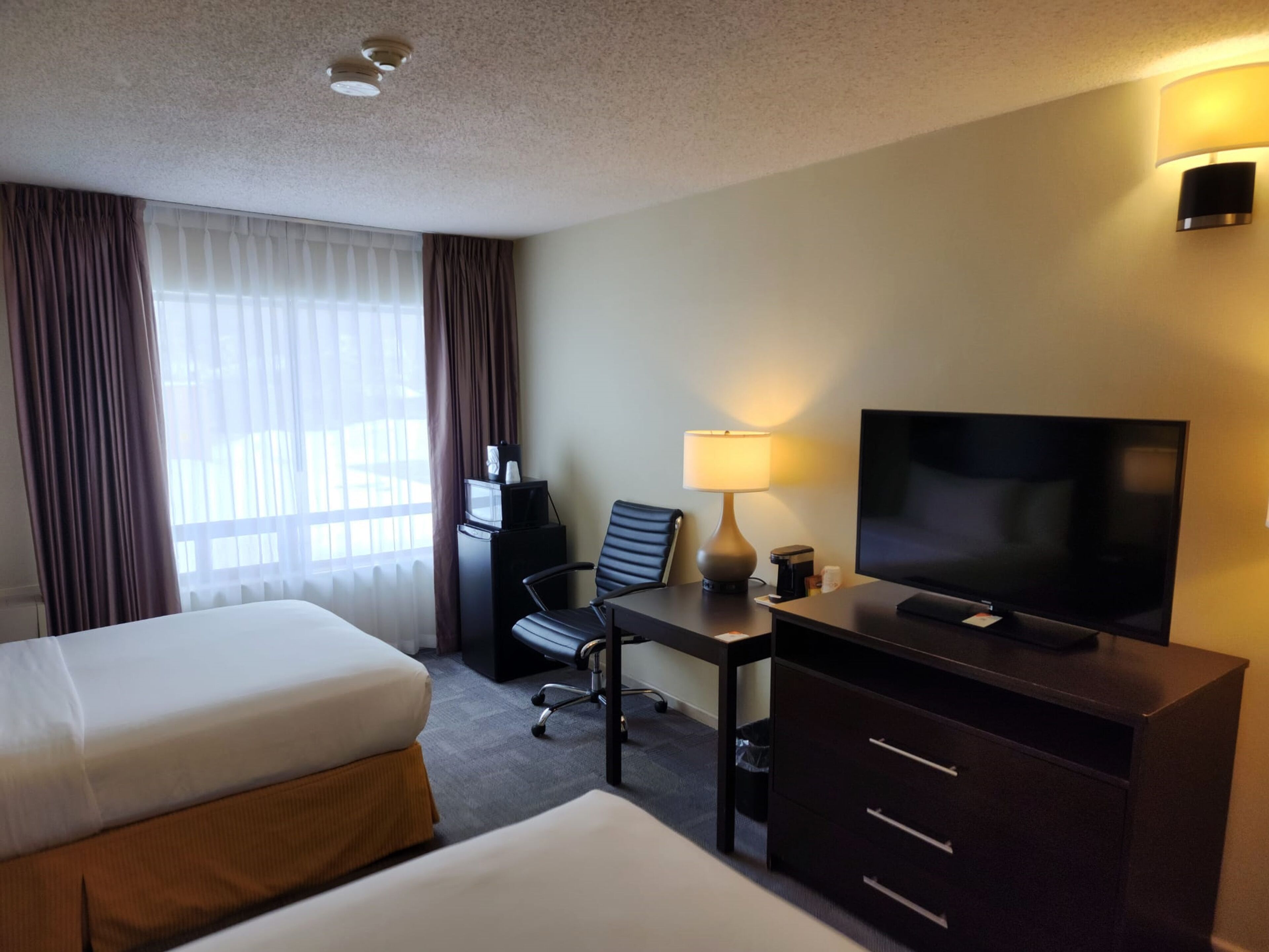 Habitación de hotel con cama, escritorio con televisor, silla, lámpara y minibar.