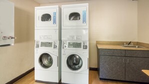A laundry room with two stacked front-loading washing machines, a sink, and a cabinet. - Red Roof Inn Durham - Triangle Park (Durham)