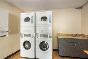 Une buanderie équipée de deux machines à laver à chargement frontal superposées, d’un évier et d’un meuble de rangement.