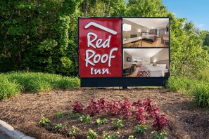 Placa da Red Roof Inn com vista para um quarto que tem uma cama, uma mesa e uma cadeira.