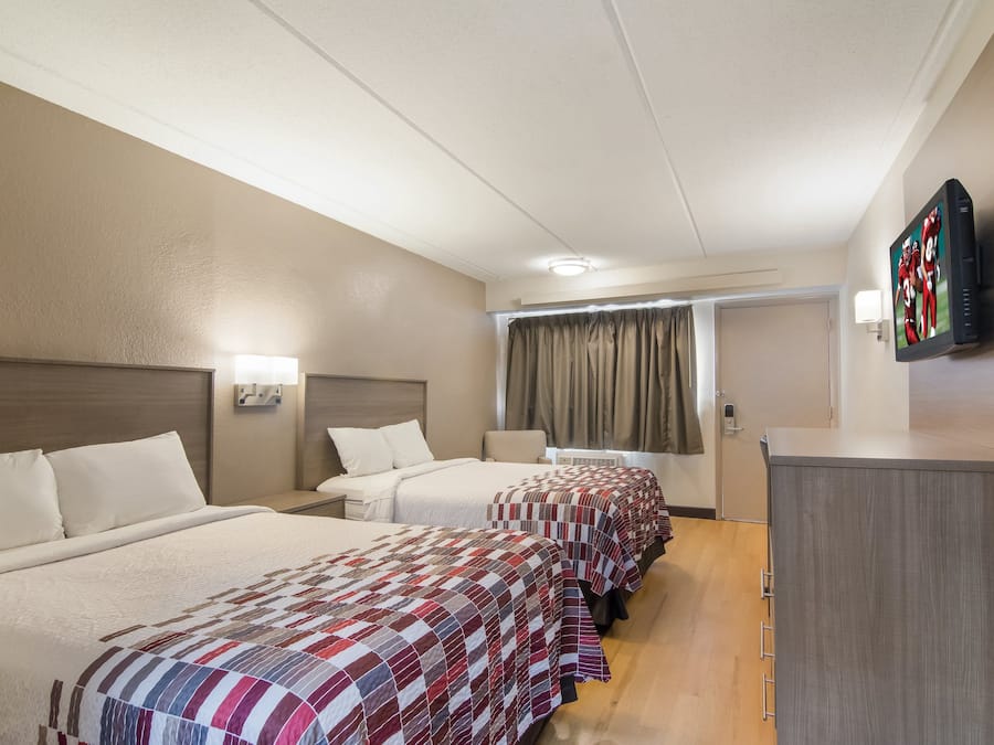 A hotel room with a long bed, a desk, a television, and a window with curtains.