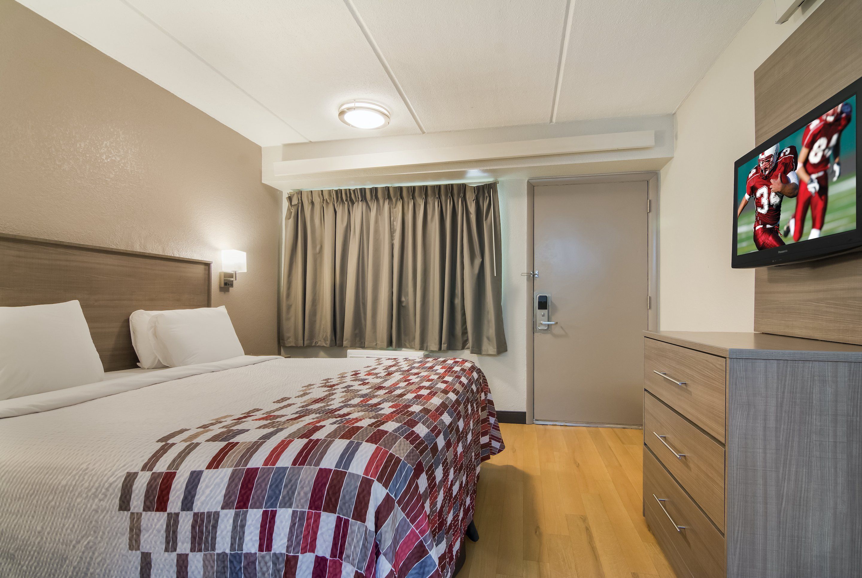 A hotel room with a bed, a television, a desk, and a door.