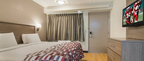 A hotel room with a bed, a television, a desk, and a door.