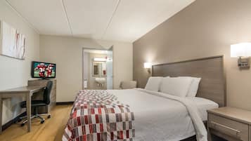 A hotel room with a bed, desk, chair, television, and a bathroom visible through an open door.