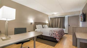 A hotel room with a bed, desk, chair, lamp, and a television on the wall.