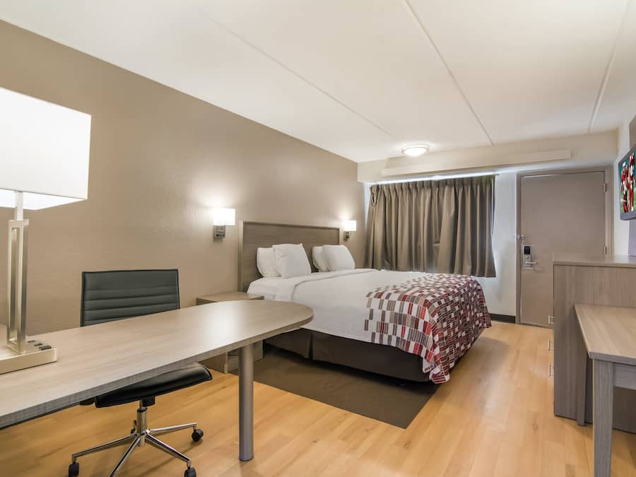 Een hotelkamer met een bed, bureau, stoel, lamp en een televisie aan de muur.