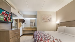 A hotel room with a bed, a TV on a dresser, a mirror, and a painting on the wall. - Red Roof Inn Durham - Triangle Park (Durham)