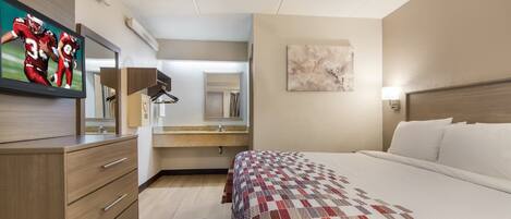 Habitación de hotel con cama, televisión, escritorio y espejo de baño.