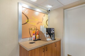 Un comptoir d’accueil avec une machine à café, une poubelle et un mur orné d’une citation inspirante.