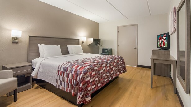 A hotel room with a bed, bedside tables, a television, and a door. - Red Roof Inn Durham - Triangle Park (Durham)