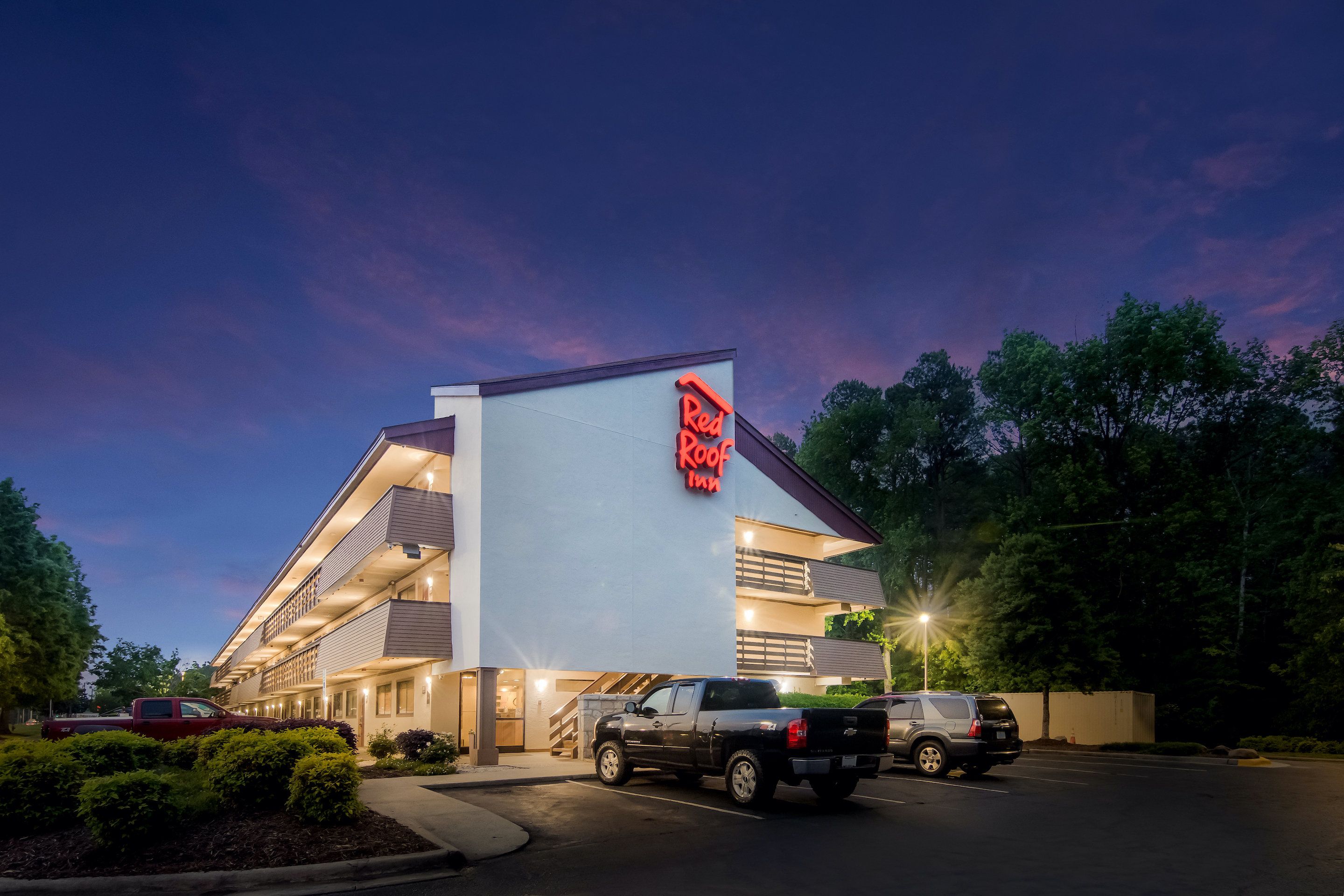 A Red Roof Inn with a modern design, featuring a prominent red sign, a parking lot with several vehicles, and a well-lit entrance.