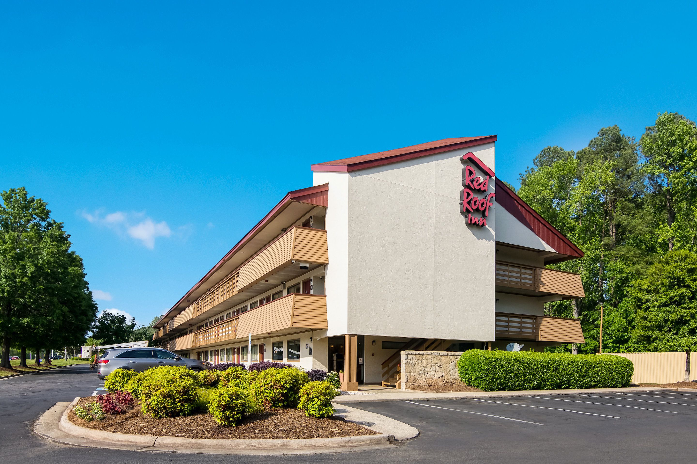Un hotel Red Roof Inn con diseño moderno, que destaca por un letrero rojo y blanco, un estacionamiento y jardines cuidados.