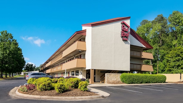 A Red Roof Inn with a modern design, featuring a prominent red and white sign, a parking lot, and landscaped greenery. - Red Roof Inn Durham - Triangle Park (Durham)